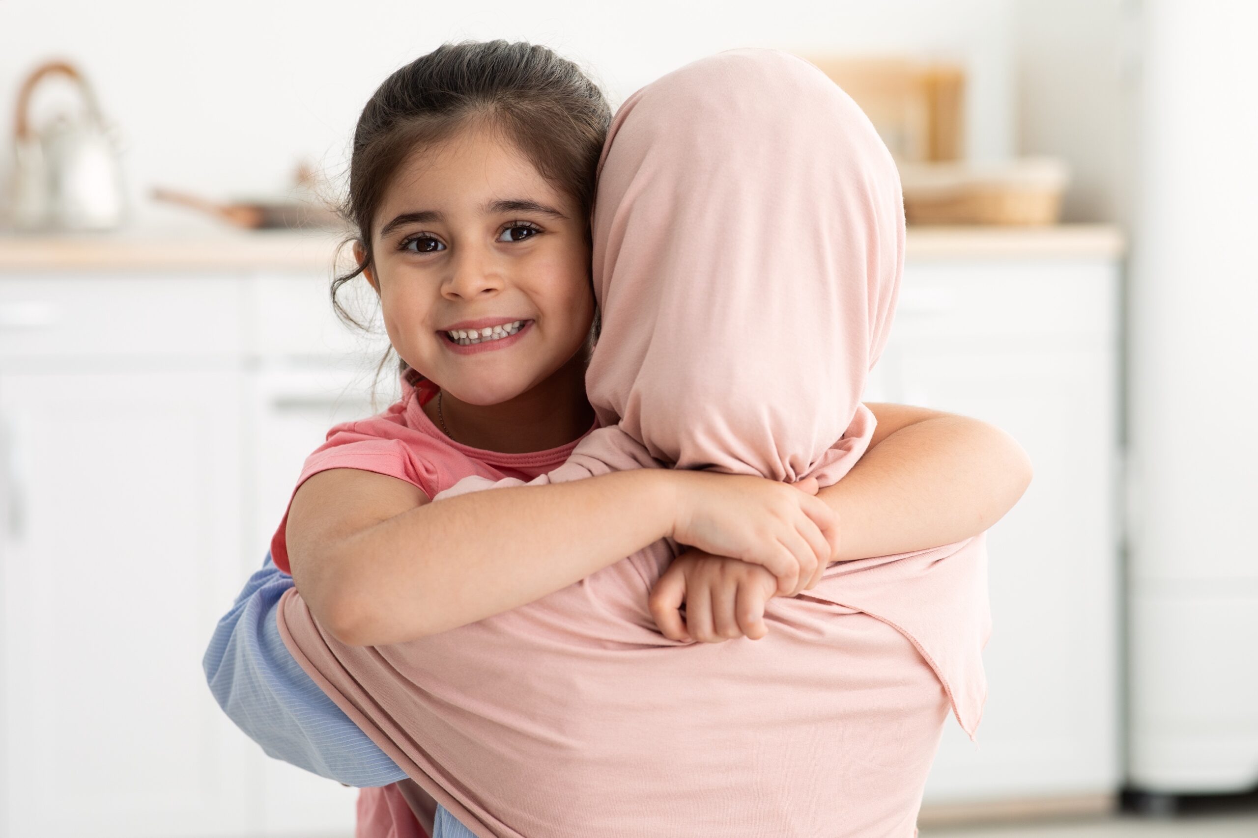 Love My Mommy. Cute Little Girl Embracing Her Islamic Mom In Hijab And Smiling At Camera, Happy Female Kid Cuddling Muslim Mother, Enjoying Spending Time Together At Home, Closeup With Free Space