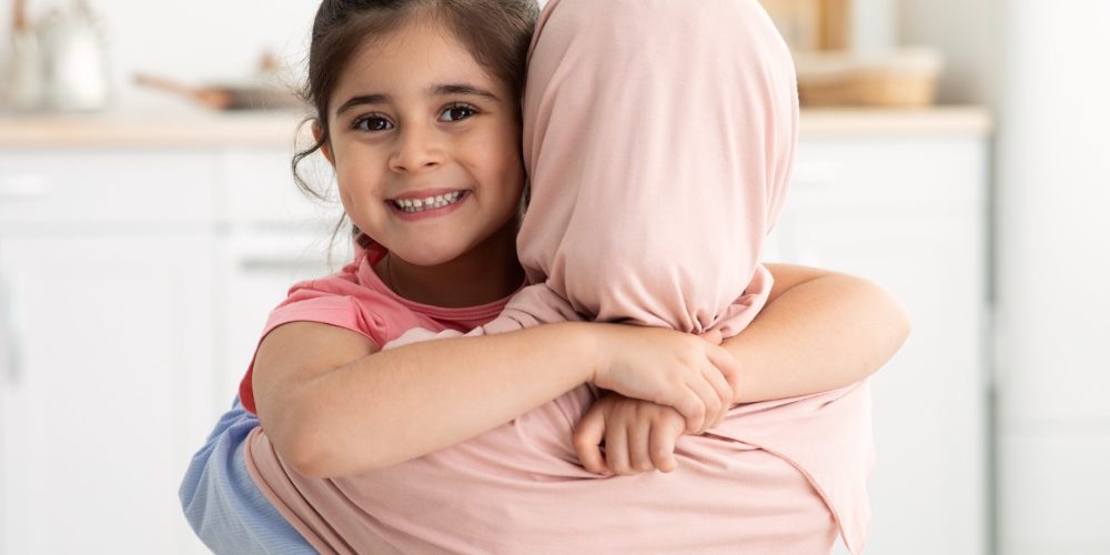 Love My Mommy. Cute Little Girl Embracing Her Islamic Mom In Hijab And Smiling At Camera, Happy Female Kid Cuddling Muslim Mother, Enjoying Spending Time Together At Home, Closeup With Free Space